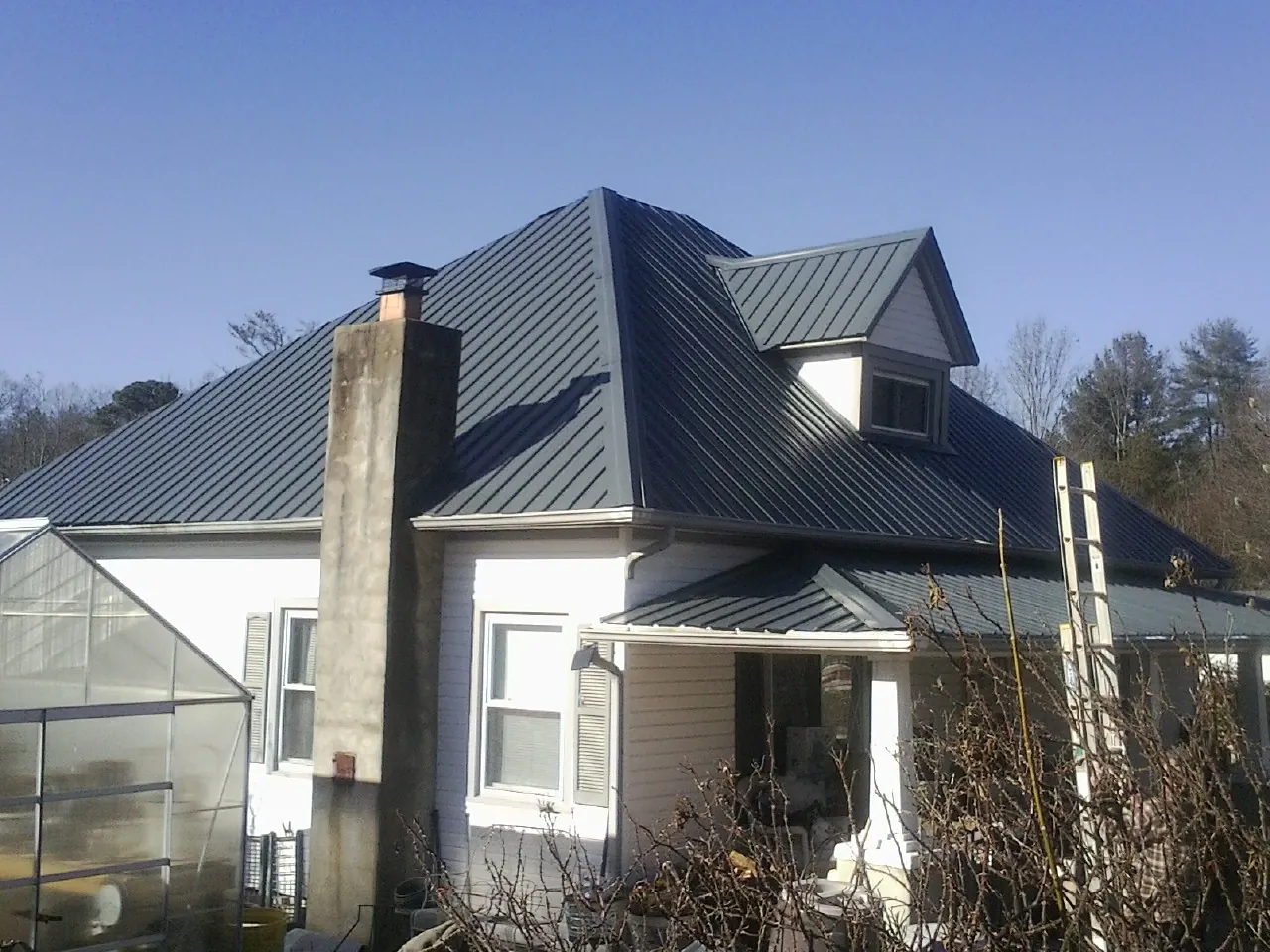 Dark blue standing seam metal roof on a white farmhouse with dormer — Slate & Tile Roof Repair by Roofing Brothers in Lake Delton