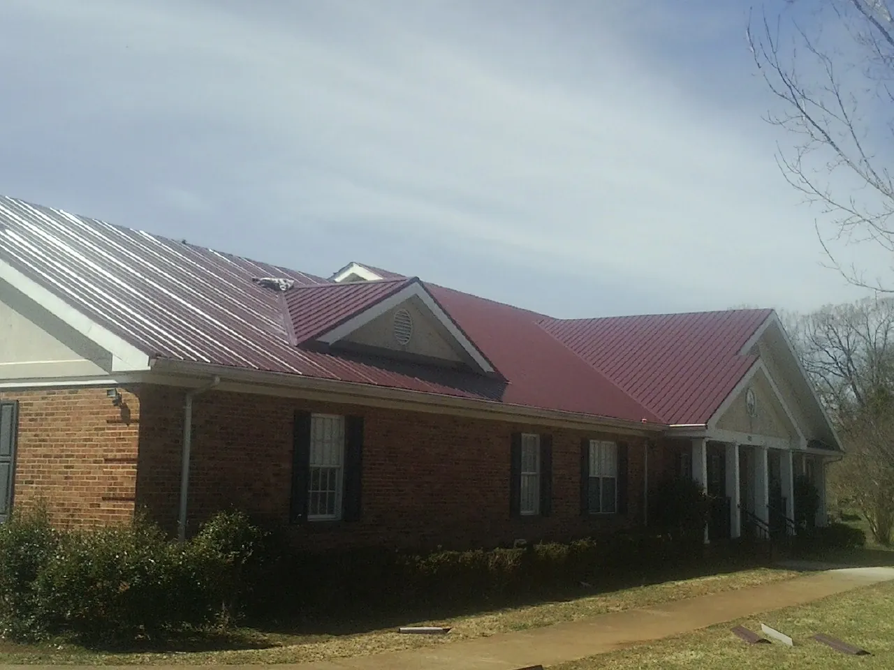 Red metal roof with gabled entries on a long brick building, from a Hail Damage Roof Repair job in Lake Delton