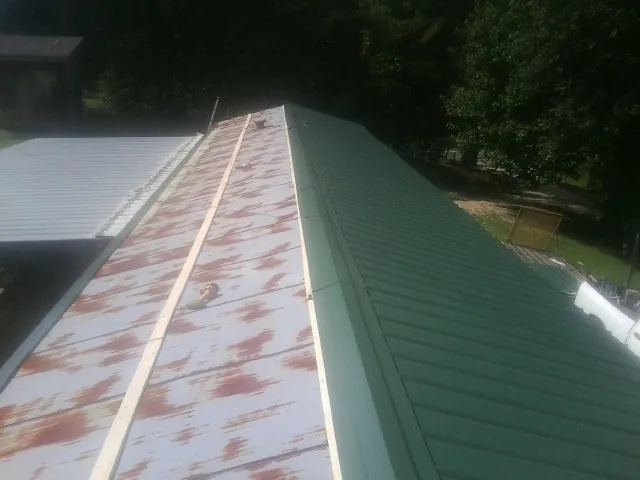 Old rusted panels beside newly installed green metal roofing — Wind Damage Roof Repair by Roofing Brothers in Lake Delton
