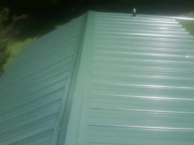 New green metal panels meeting at the ridge of a roof — Flat Roof Repair work by our crew in Lake Delton