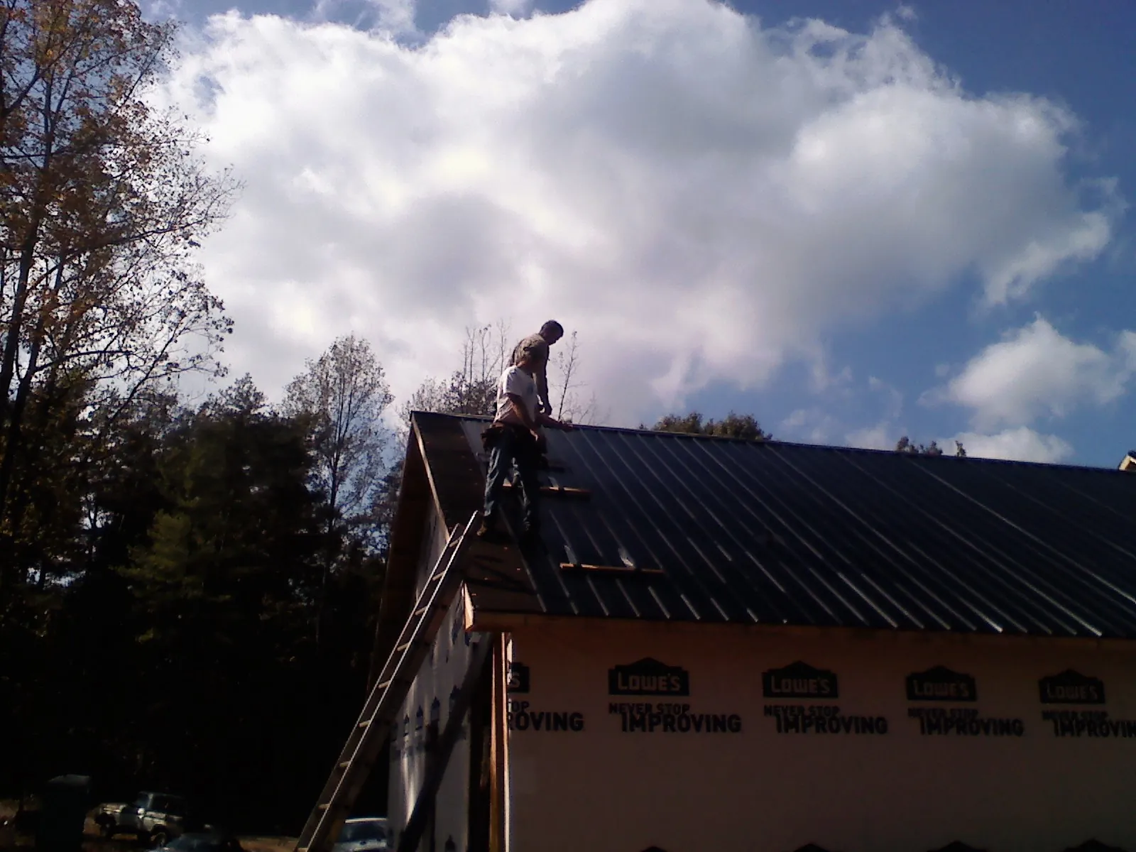 Roofer fastening dark metal panels high against a cloudy sky, from a Roof Inspection job in Lake Delton
