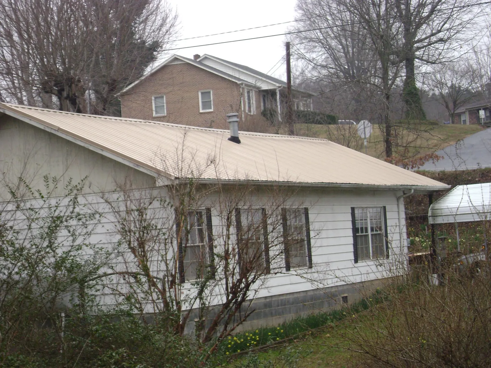 Tan metal roof on a white sided house set into a hillside — Commercial Roofing by Roofing Brothers in Lake Delton